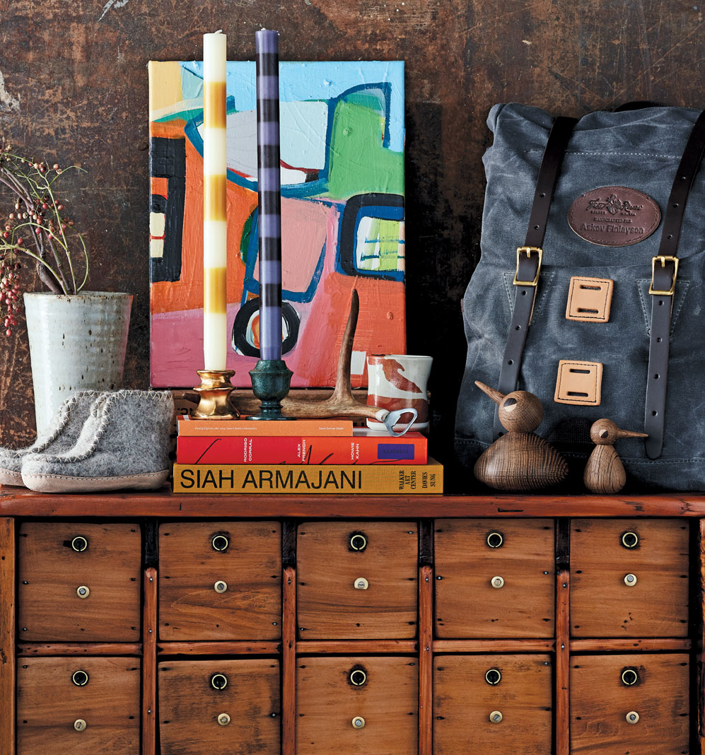A dresser with various gifts found in the Holiday Gift Guide placed on top, including shoes, candles, a vase, and more.