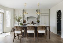 Enduring Elegance: A Timeless and Functional Kitchen Remodel Packed with custom cabinetry, the kitchen is the heart of the home. The warm oak island, accented by Ormandy pendant lights from Rejuvenation, anchors the space and provides contrast with the walls and millwork, painted in Benjamin Moore’s creamy Swiss Coffee shade.