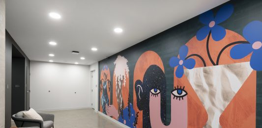 An apartment building hallway featuring a mural with graphic shapes and whimsical design with bold, bright colors.