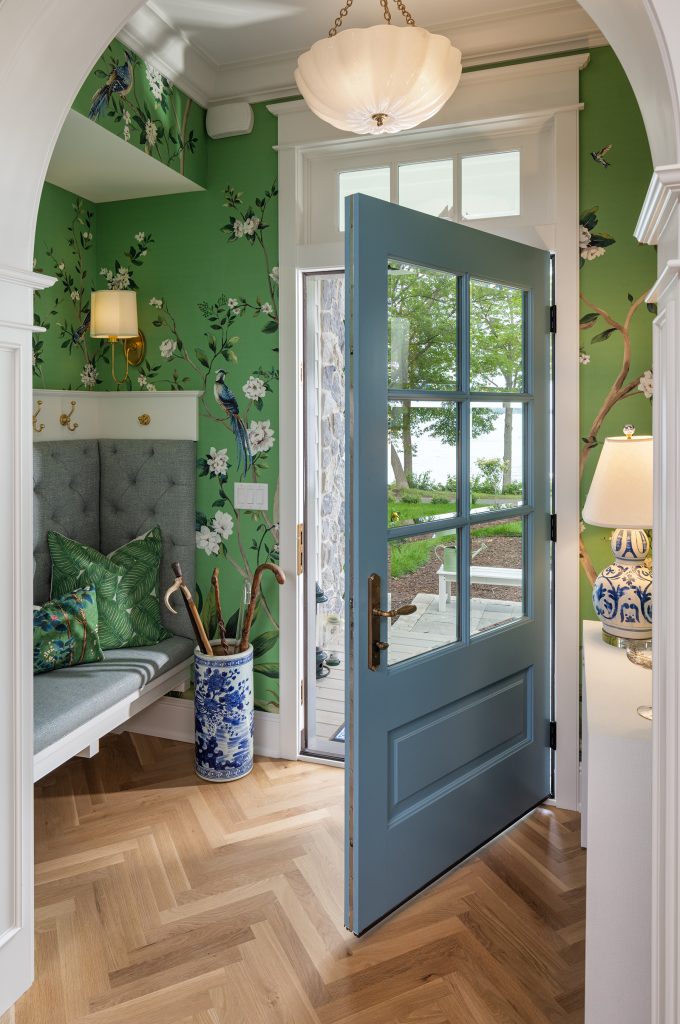 This bold foyer has green patterned wallpaper and a blue door, showing off the homeowners' personality. 