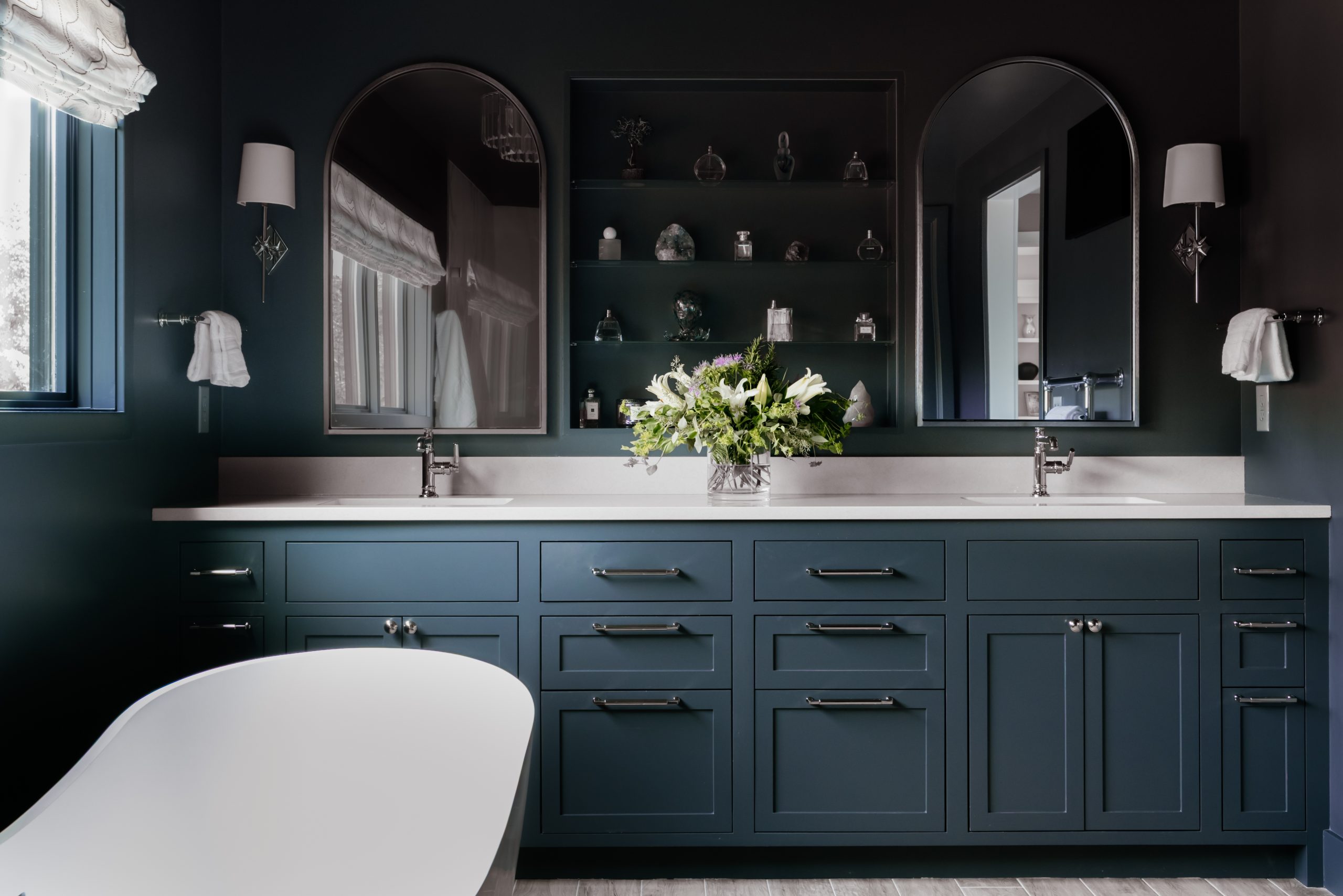 Painted in Sherwin- Williams’ striking Cyberspace shade, the color-drenched primary bath features faux onyx tile in the shower and a soaking tub suspended among washed river rocks for an earthy addition. 